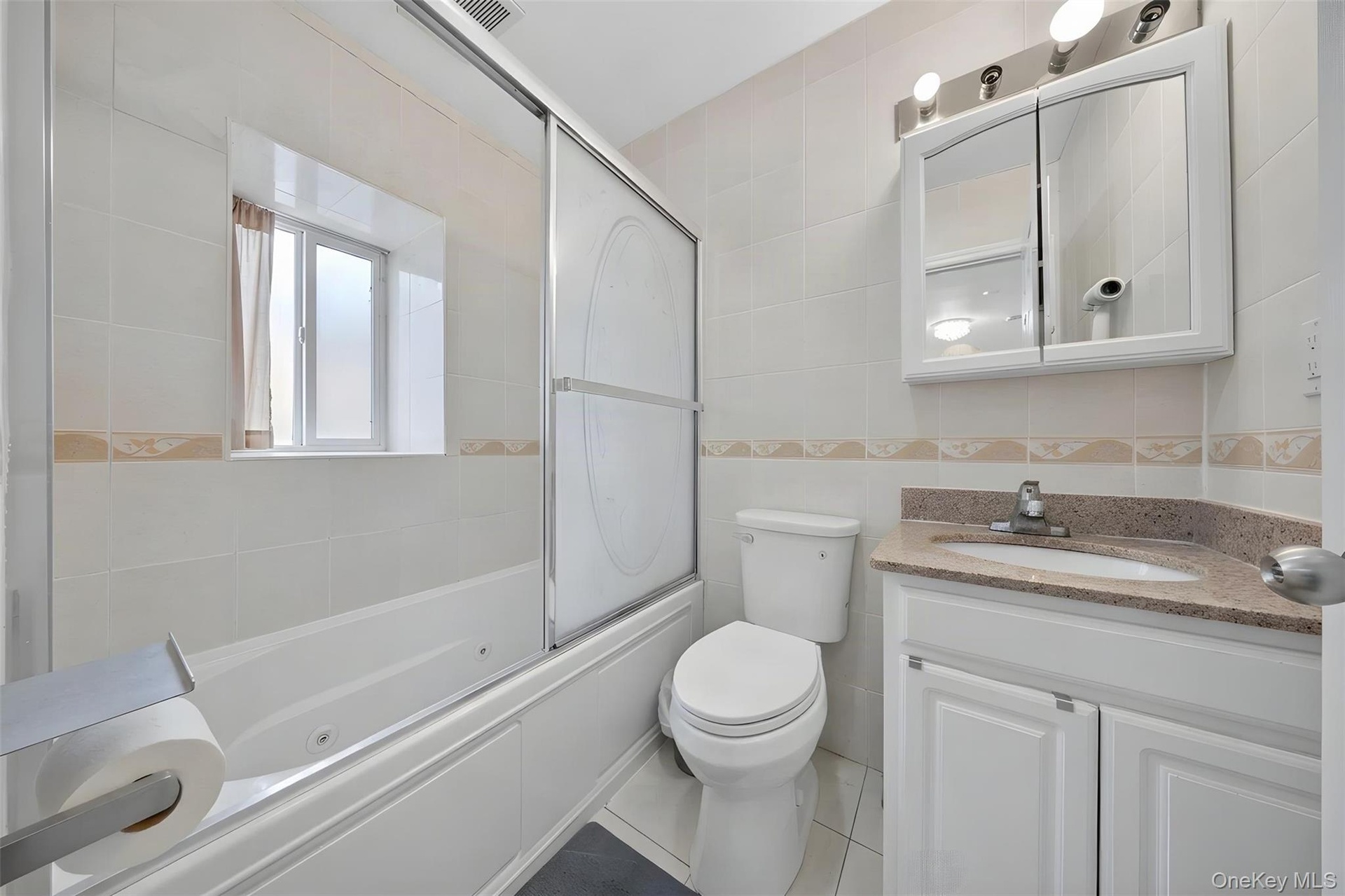 Tiled bathroom featuring a built-in bathtub with sliding glass doors, white vanity with a light-colored countertop, and a wall-mounted medicine cabine
