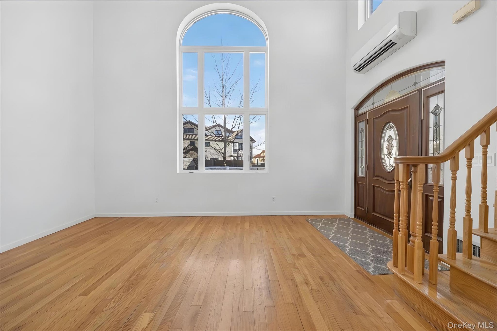 Bright, light-filled foyer showcasing warm wood-finish flooring, an arched transom window with natural light, and an elegant wooden staircase with dec