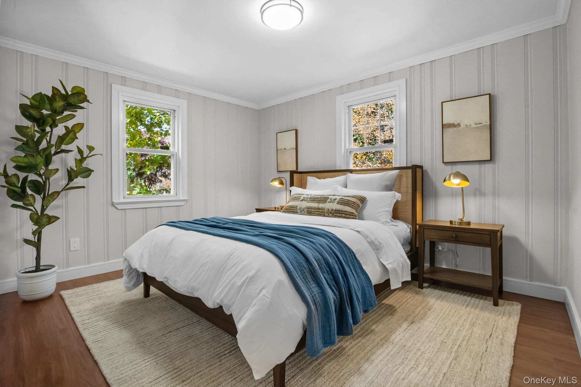Bright secondary bedroom with hardwood floors, crown molding, and double windows overlooking the landscaped yard.