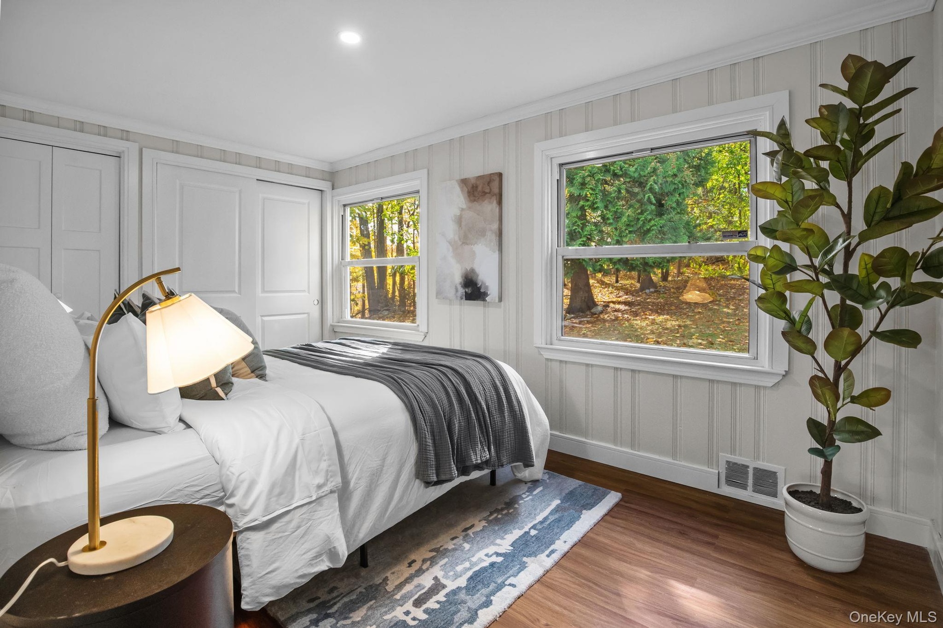 Newly renovated bedroom with warm hardwood floors and picture windows framing serene wooded views for a peaceful retreat.