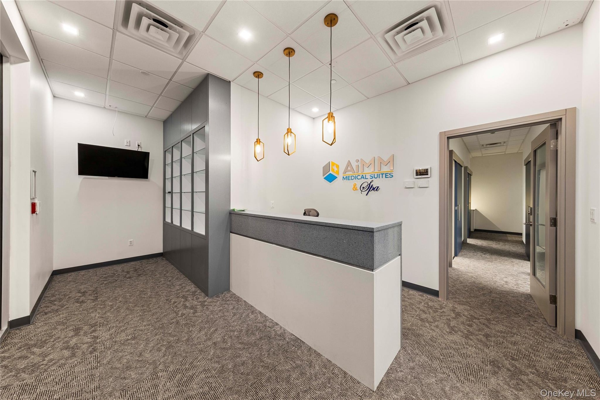 Modern reception area featuring a built-in white and gray reception desk, three gold-toned pendant lights, and textured gray carpeting