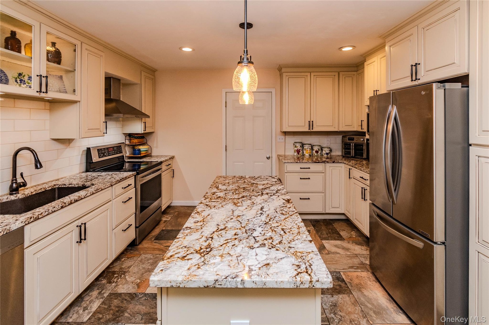 Kitchen featuring a center island with a stone surface, perimeter cabinetry with stone countertops, stainless steel appliances, a tile backsplash, and