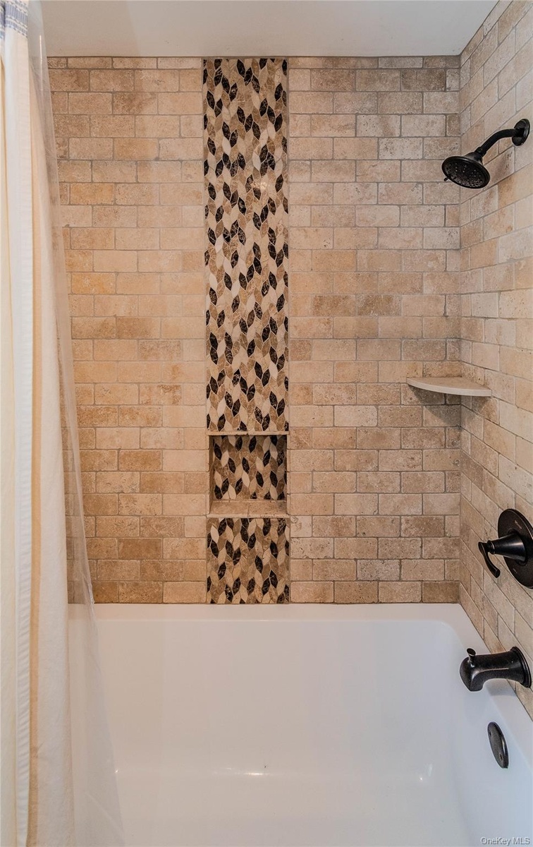 Tiled shower surround with decorative mosaic inlay, two recessed niches, and dark bronze fixtures