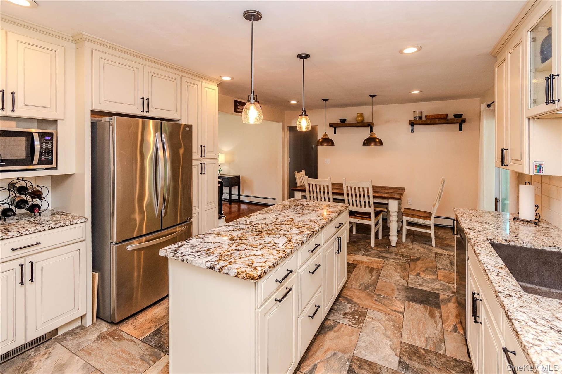 Kitchen featuring extensive cabinetry, stainless steel refrigerator, stone countertops, pendant lighting, and stone tile flooring