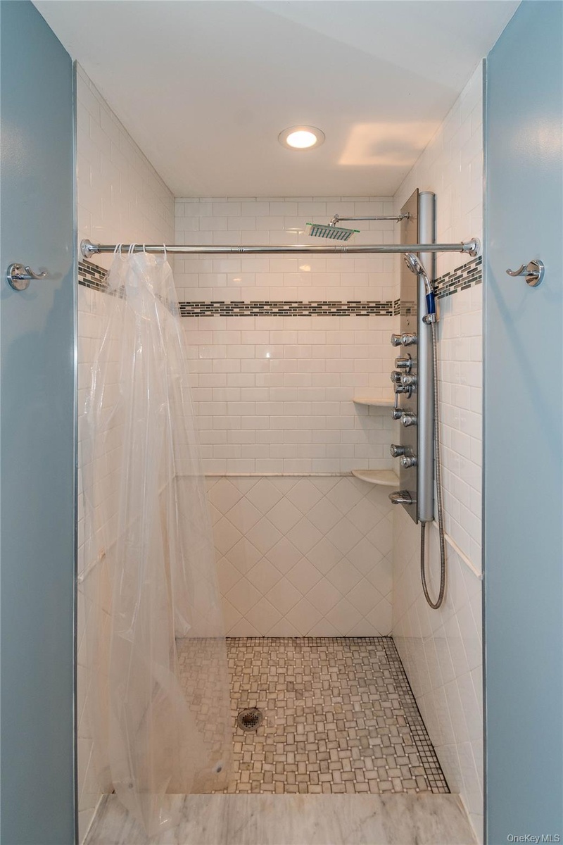 Shower featuring white subway tile walls, a mosaic tile accent band, a multi-function shower panel with an overhead rainfall shower, and a white mosai