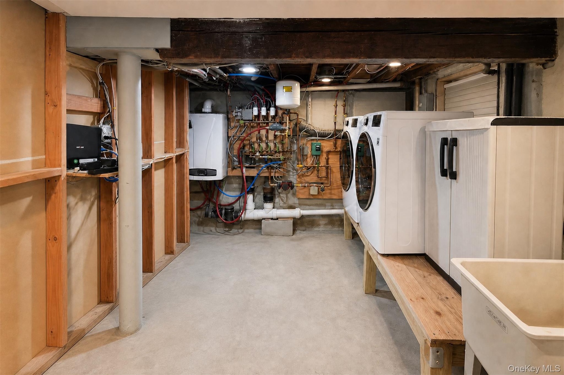 Laundry area featuring a utility sink, exposed wood support beams, and concrete flooring