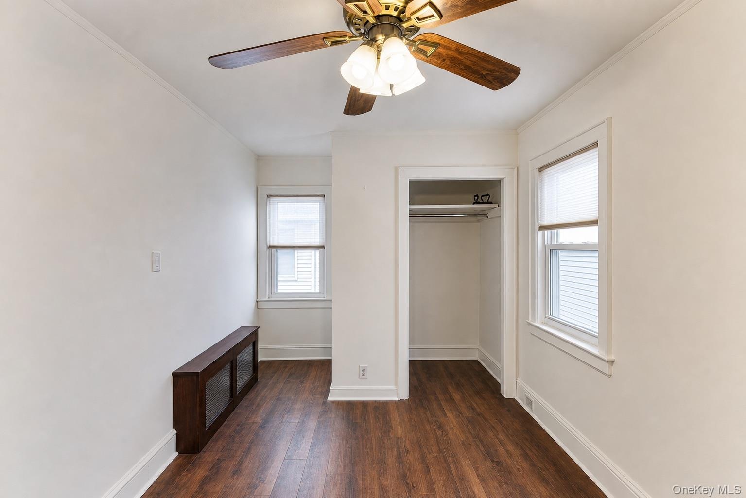 Recessed closet opening, wood-finish flooring, two windows with blinds, and ceiling fan with integrated lighting