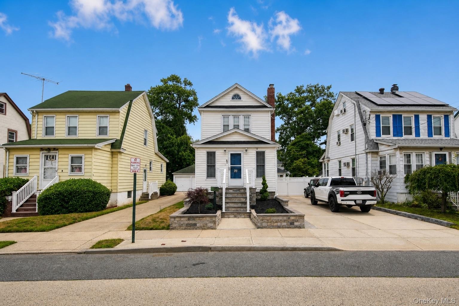 White clapboard exterior with an arched dormer, raised stone planter beds, and a concrete driveway
