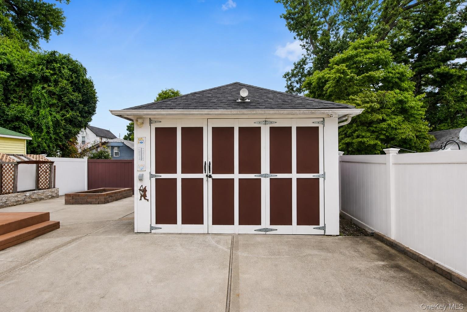 Detached garage with dark panel doors, a concrete driveway, and a white privacy fence