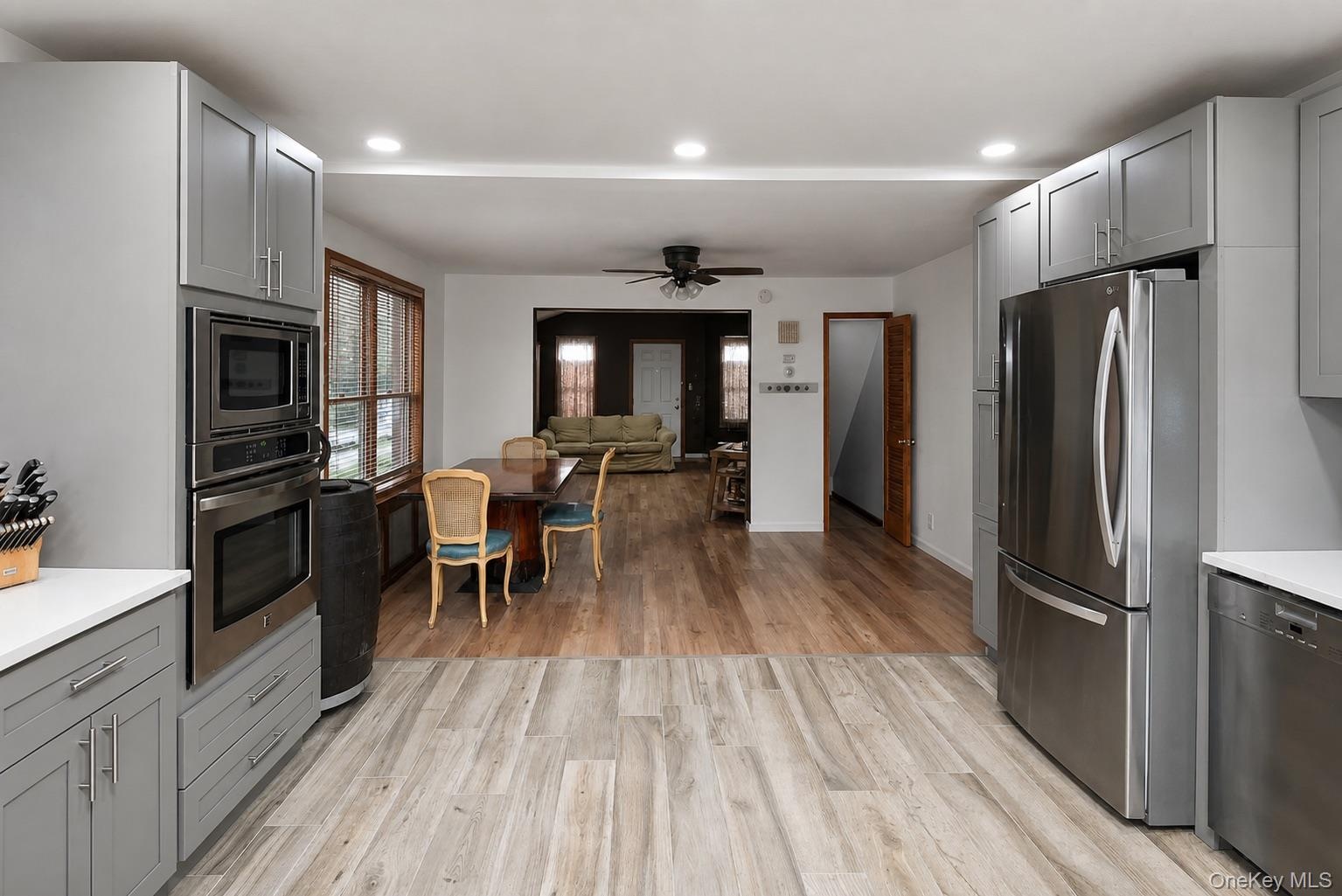 Light-toned plank flooring, gray shaker-style cabinetry, and stainless steel appliances, including a refrigerator and built-in double oven