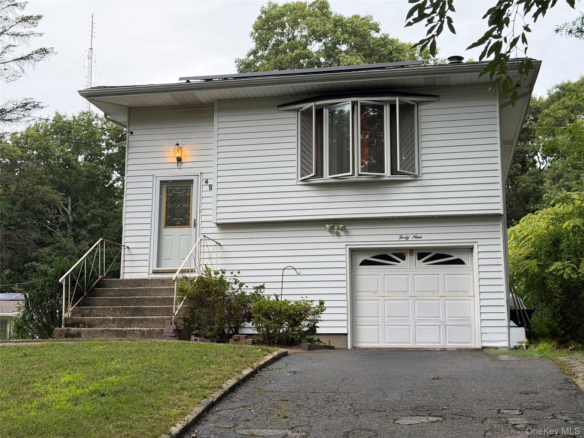 Exterior featuring white horizontal siding, a bay window with multiple panes, a white garage door with decorative lites, and a paved driveway
