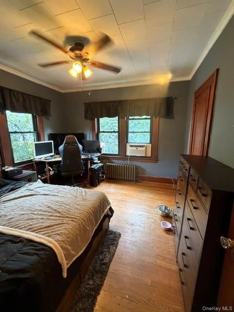 Room featuring wood-finish flooring, multiple windows, a ceiling fan with integrated lighting, and a radiator heating unit. Apt. #1