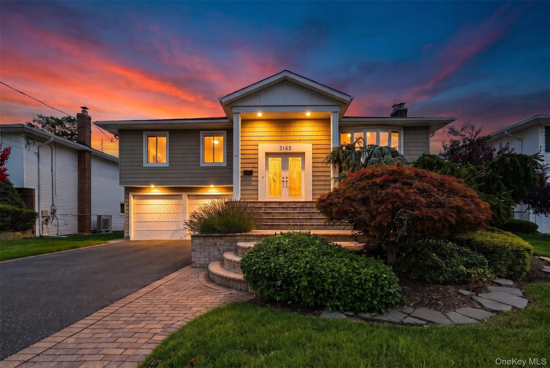 Split-level residence featuring siding exterior, an attached two-car garage, paved driveway, and a brick paver walkway leading to the front entry step
