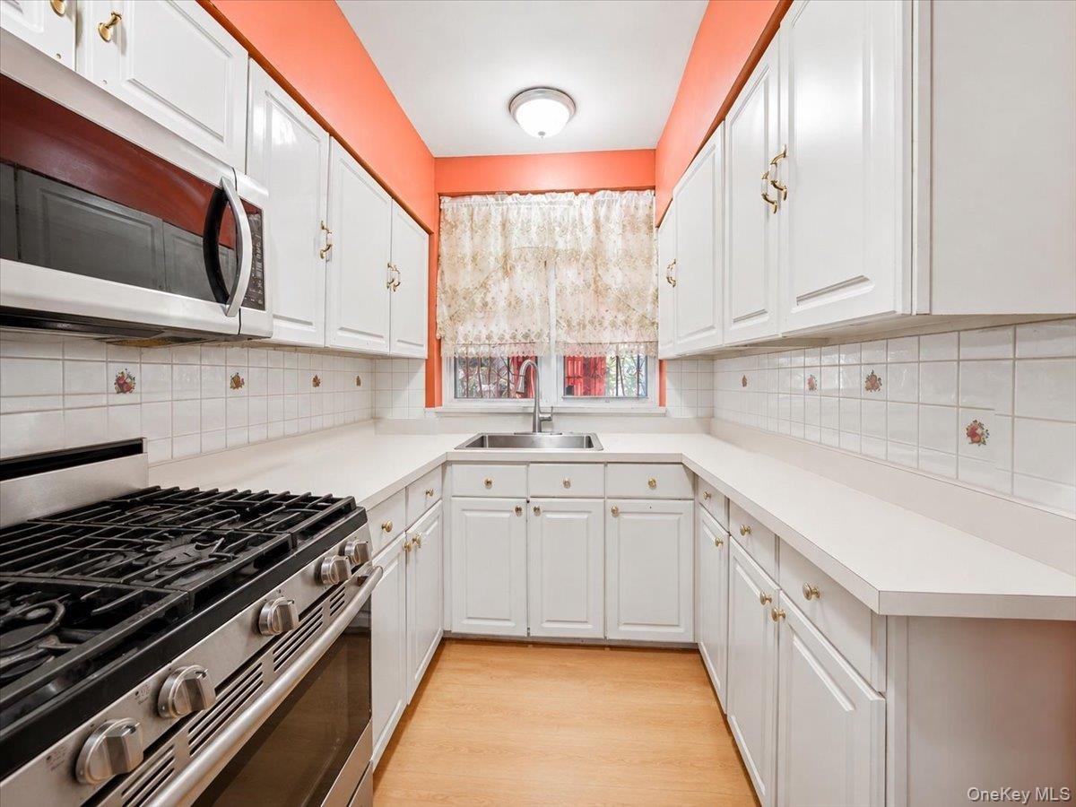 Galley kitchen featuring white cabinetry, light countertops, tile backsplash, stainless steel range, and an integrated microwave