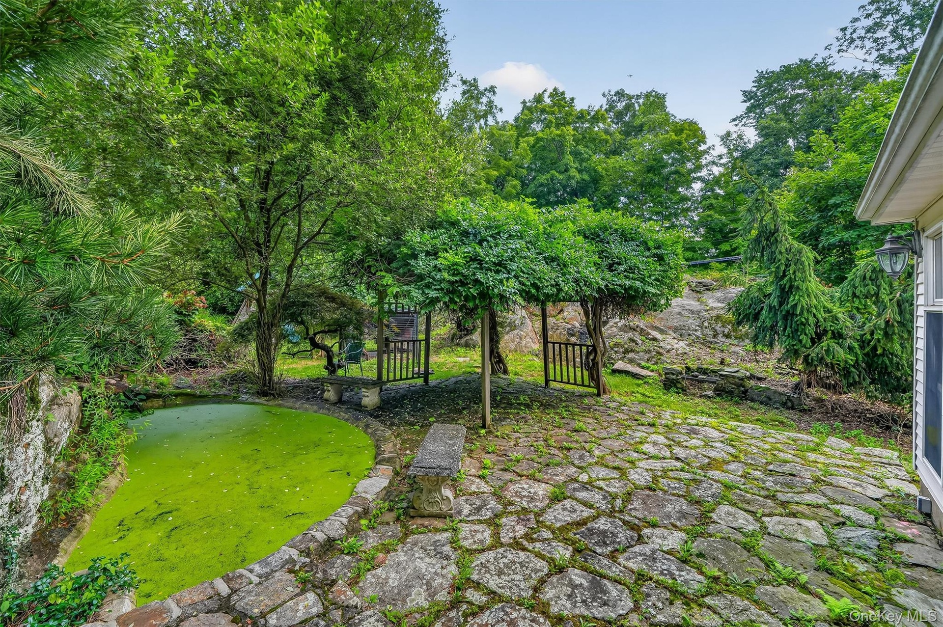 Stone paver patio with natural rock accents, surrounded by mature trees and lush landscaping