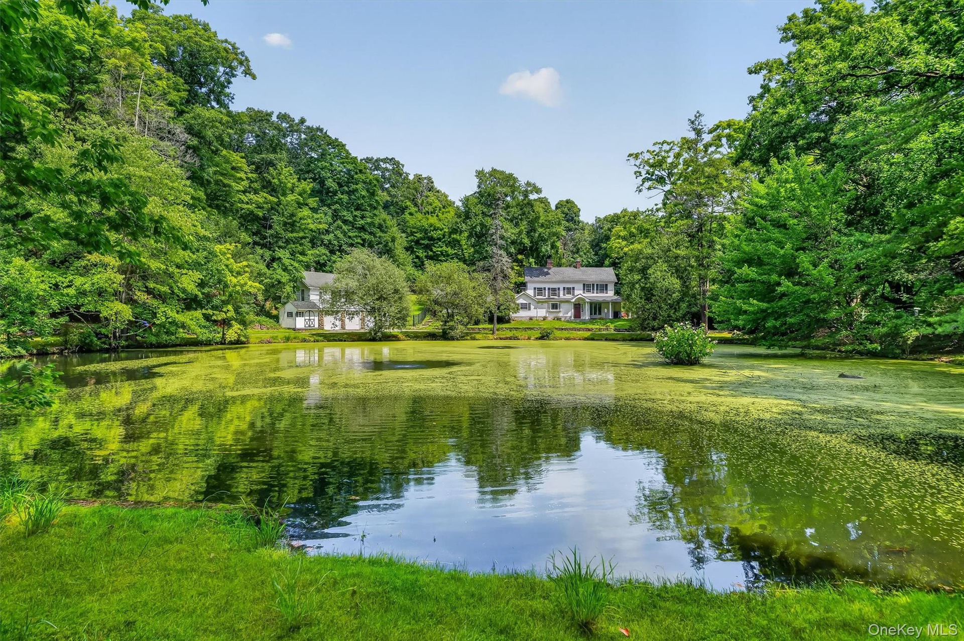 Expansive waterfront property with a white-sided two-story residence, surrounded by mature trees and lush green landscaping