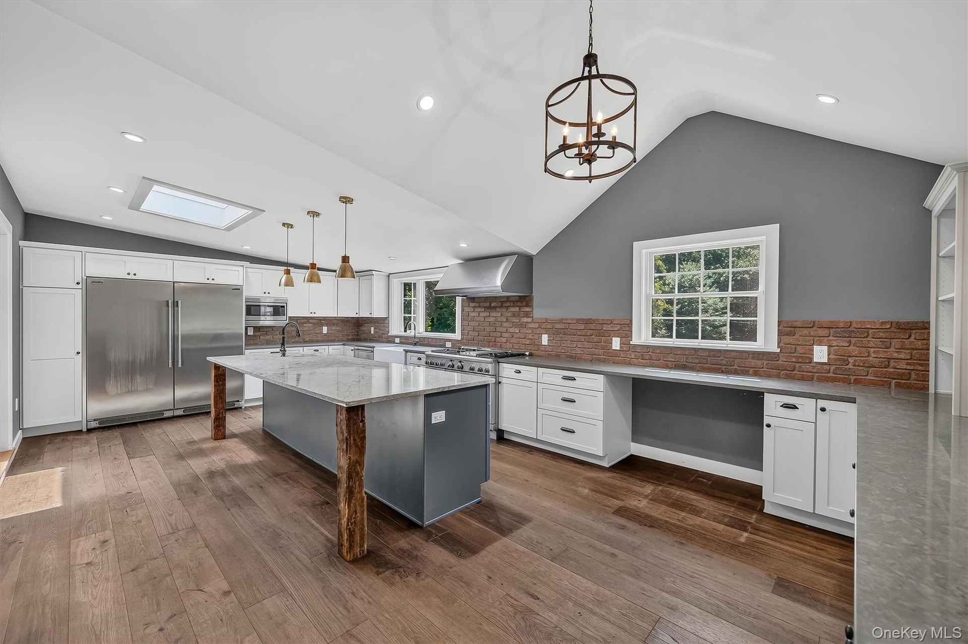 Vaulted ceiling kitchen featuring wood-finish flooring, a skylight, and an expansive island with a stone countertop. Plank Floor, Commercial grade kit