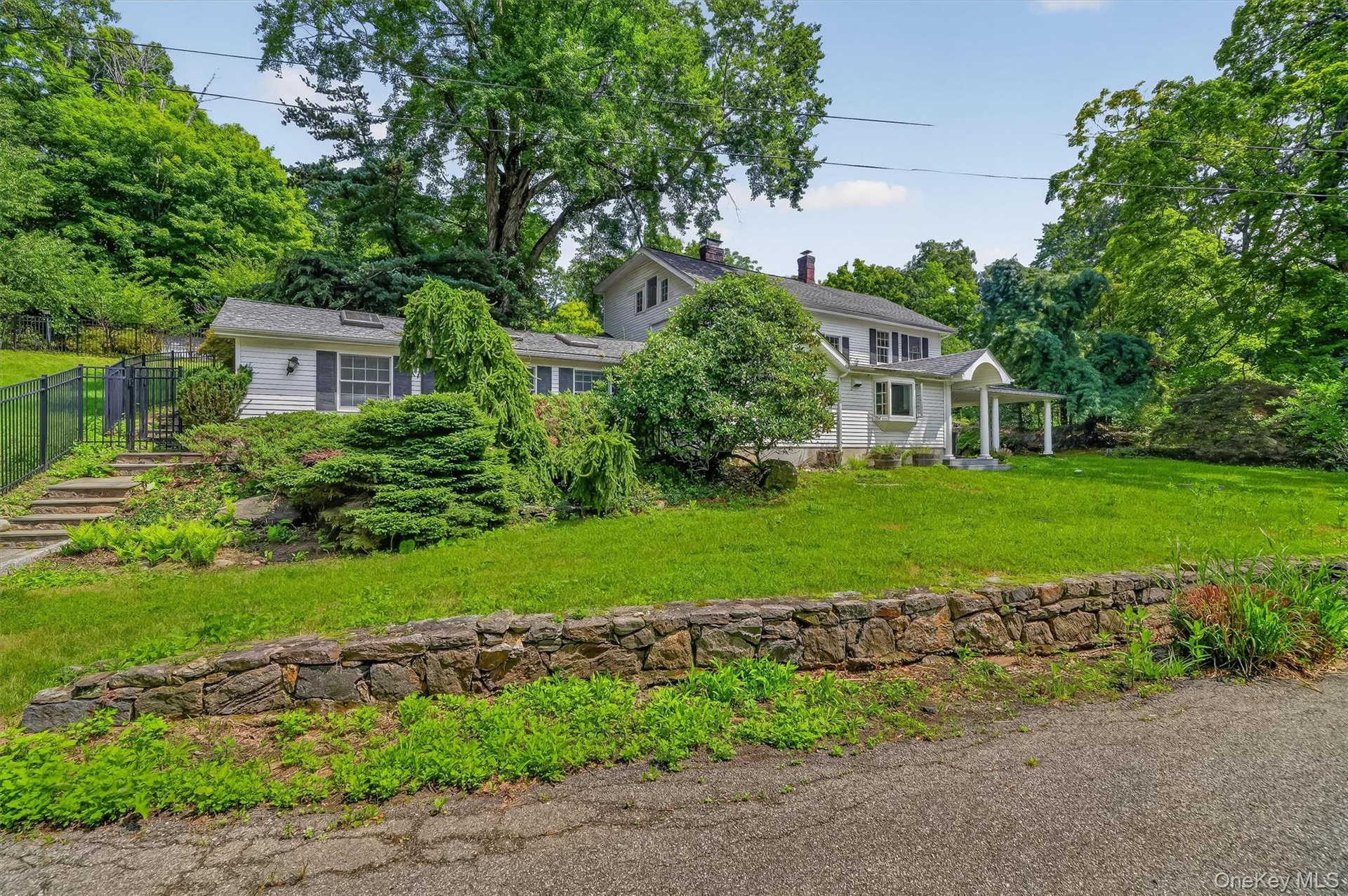 Expansive green lawn, mature trees, stone retaining wall, and a covered front porch with white columns
