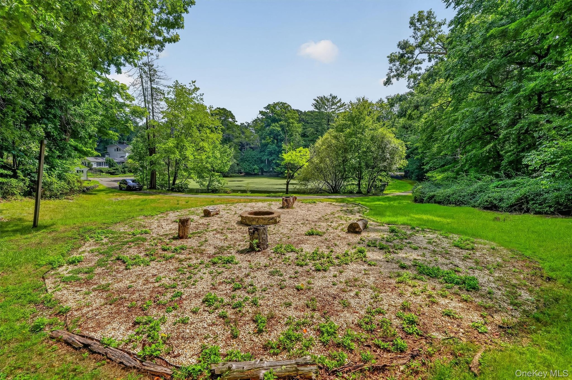 Expansive outdoor area featuring a circular gravel-covered space with tree stump seating and a stone fire pit