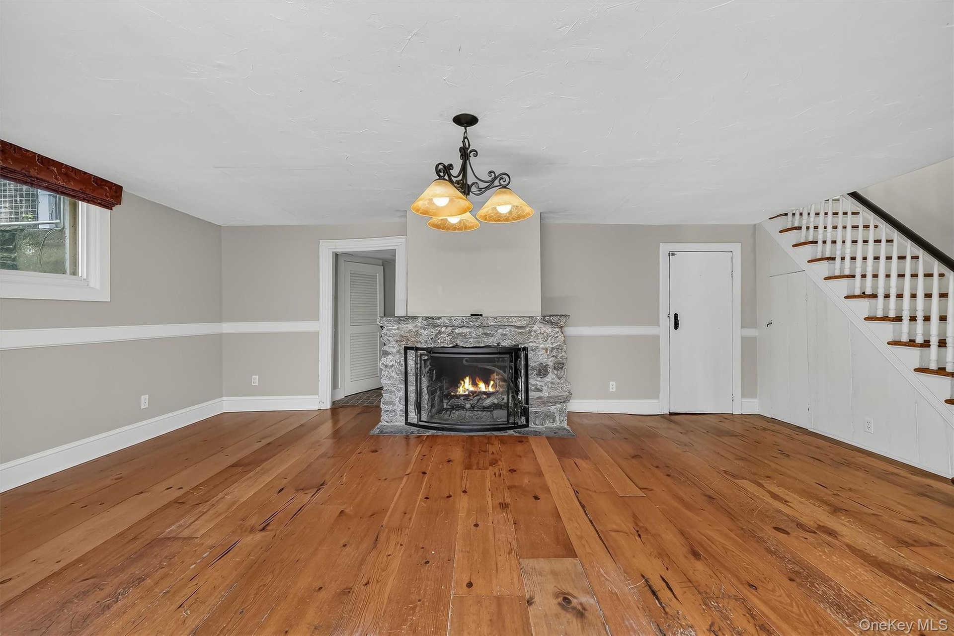 Hardwood flooring, stone fireplace, traditional chandelier, white staircase with dark wood treads, and white interior doors