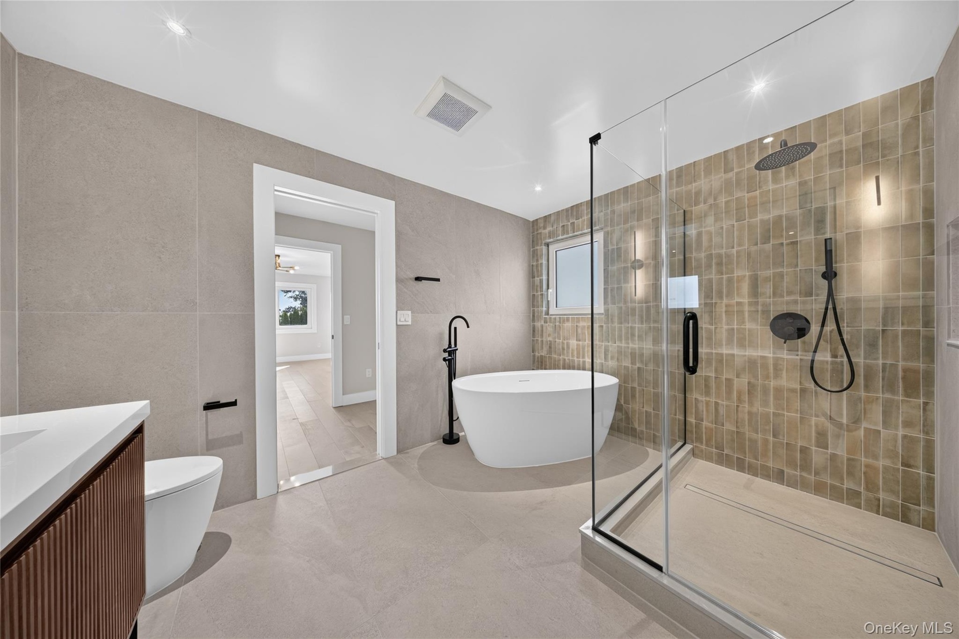 Freestanding soaking tub, glass-enclosed shower, wall-mounted showerhead, and matte black fixtures