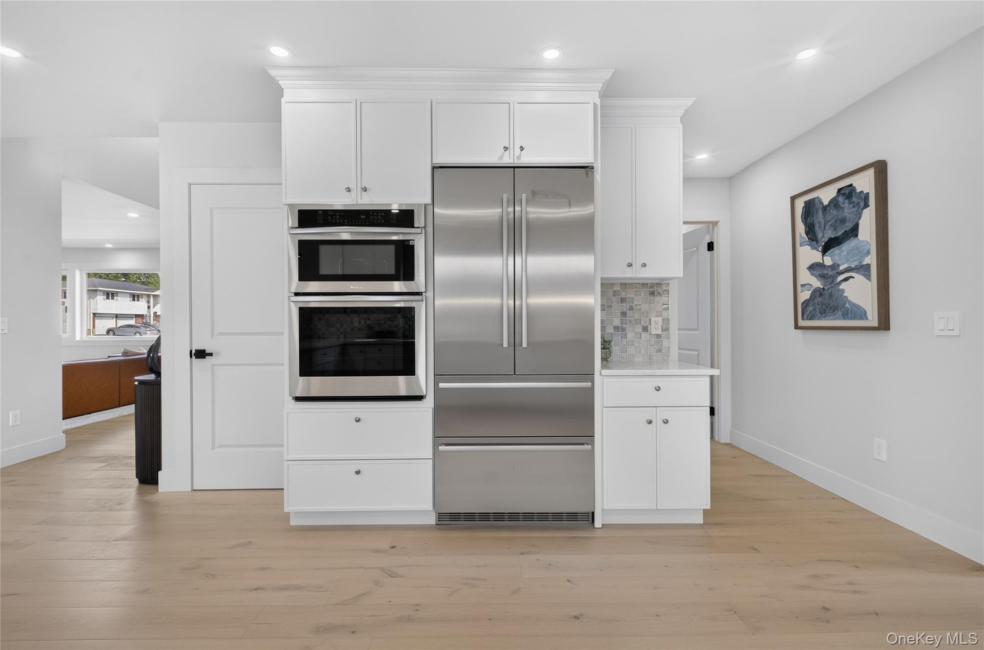 Integrated stainless steel appliances, white cabinetry with crown molding, light wood-finish flooring, and recessed lighting