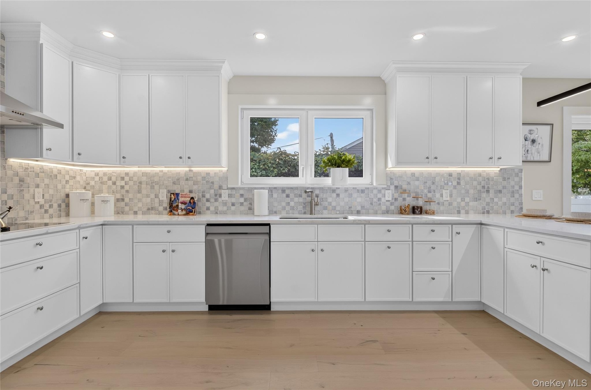 Kitchen featuring white shaker cabinetry, stainless steel appliances, mosaic tile backsplash, light wood-finish flooring, and recessed lighting