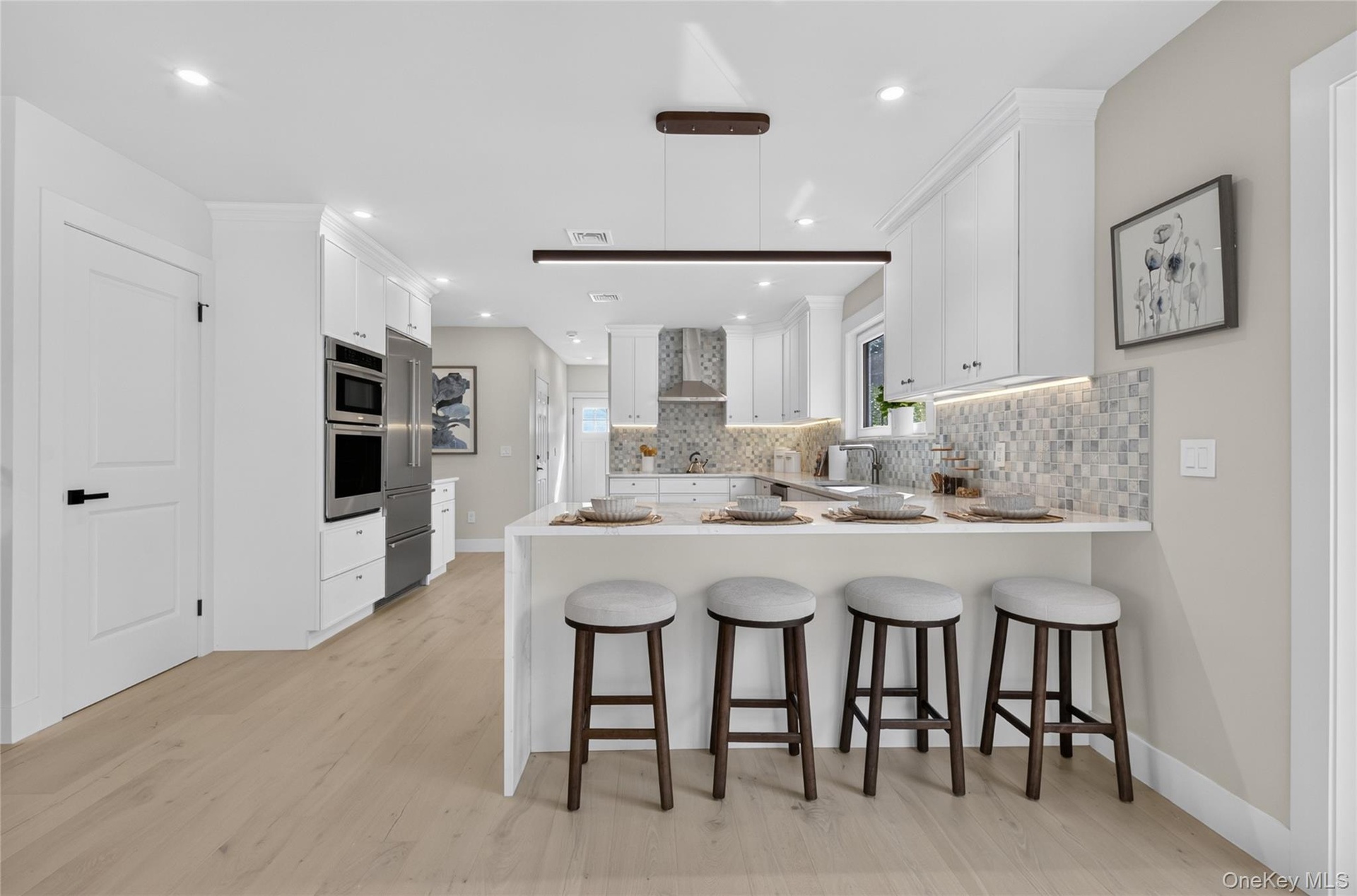 Modern kitchen featuring white cabinetry, light wood-finish flooring, stainless steel appliances, a breakfast bar, and a patterned tile backsplash