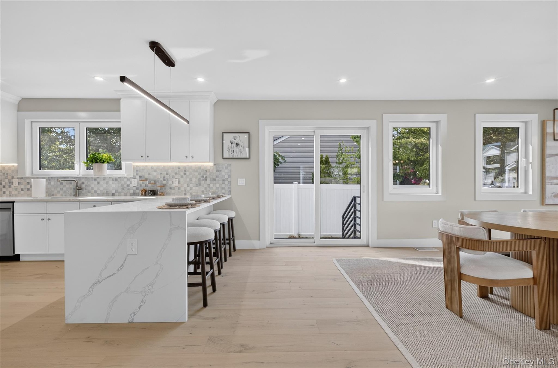 Expansive kitchen island with waterfall countertop, white shaker cabinetry, stainless steel appliances, and wood-finish flooring
