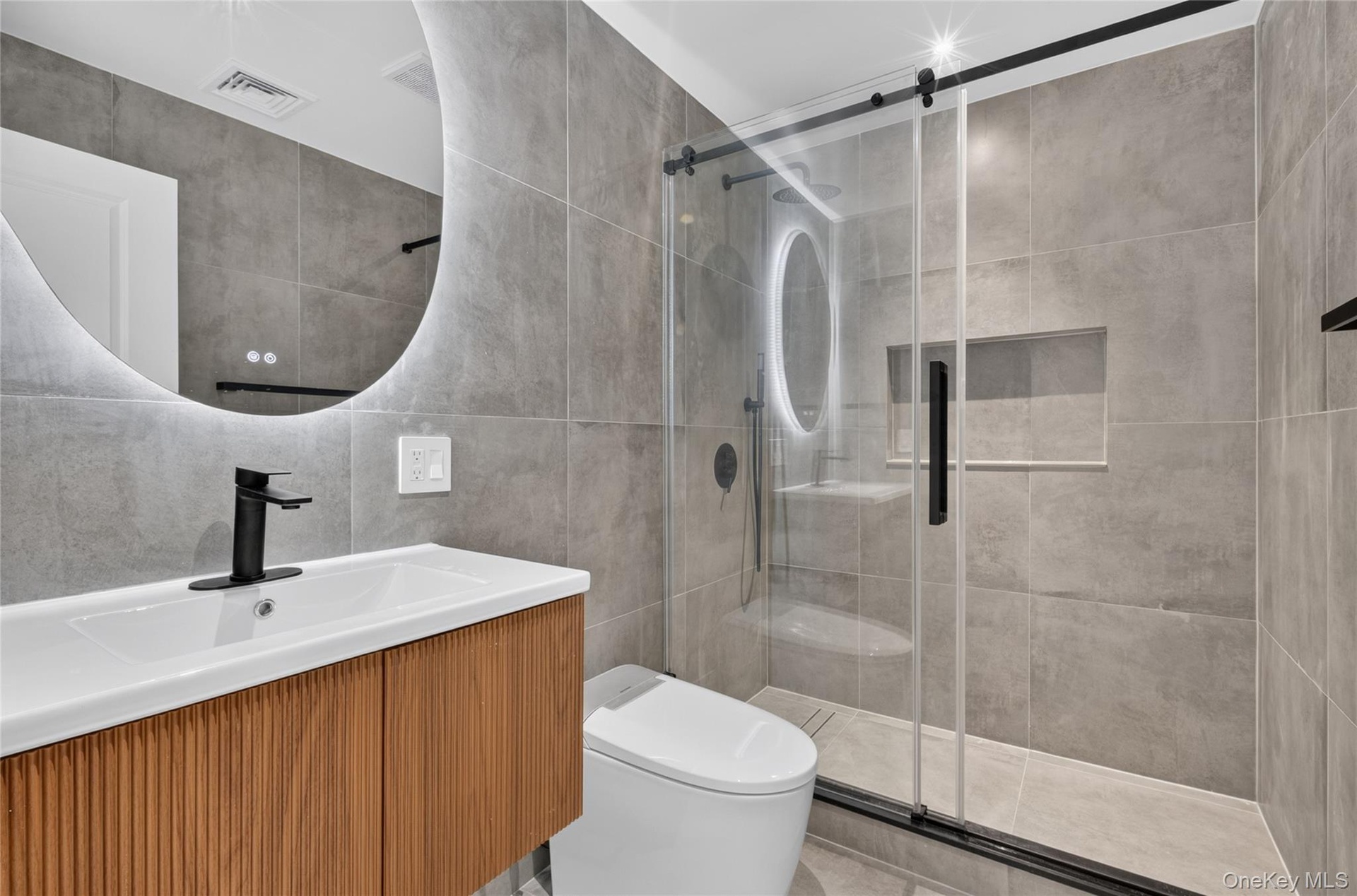 Modern bathroom featuring a wood-finish vanity, integrated sink, and an illuminated circular mirror