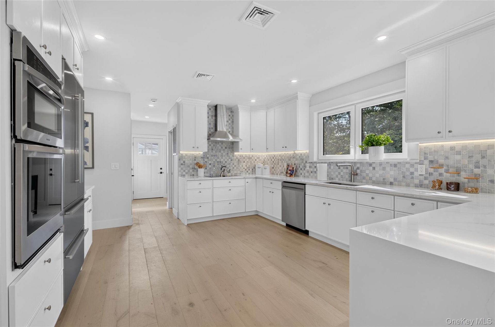 Kitchen featuring wood-finish flooring, white cabinetry, integrated stainless steel appliances, a mosaic tile backsplash, and light-toned countertops
