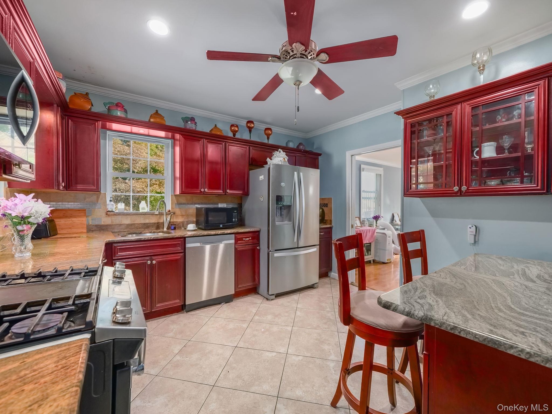 Kitchen featuring reddish brown cabinets, backsplash, appliances with stainless steel finishes, ornamental molding, and a ceiling fan