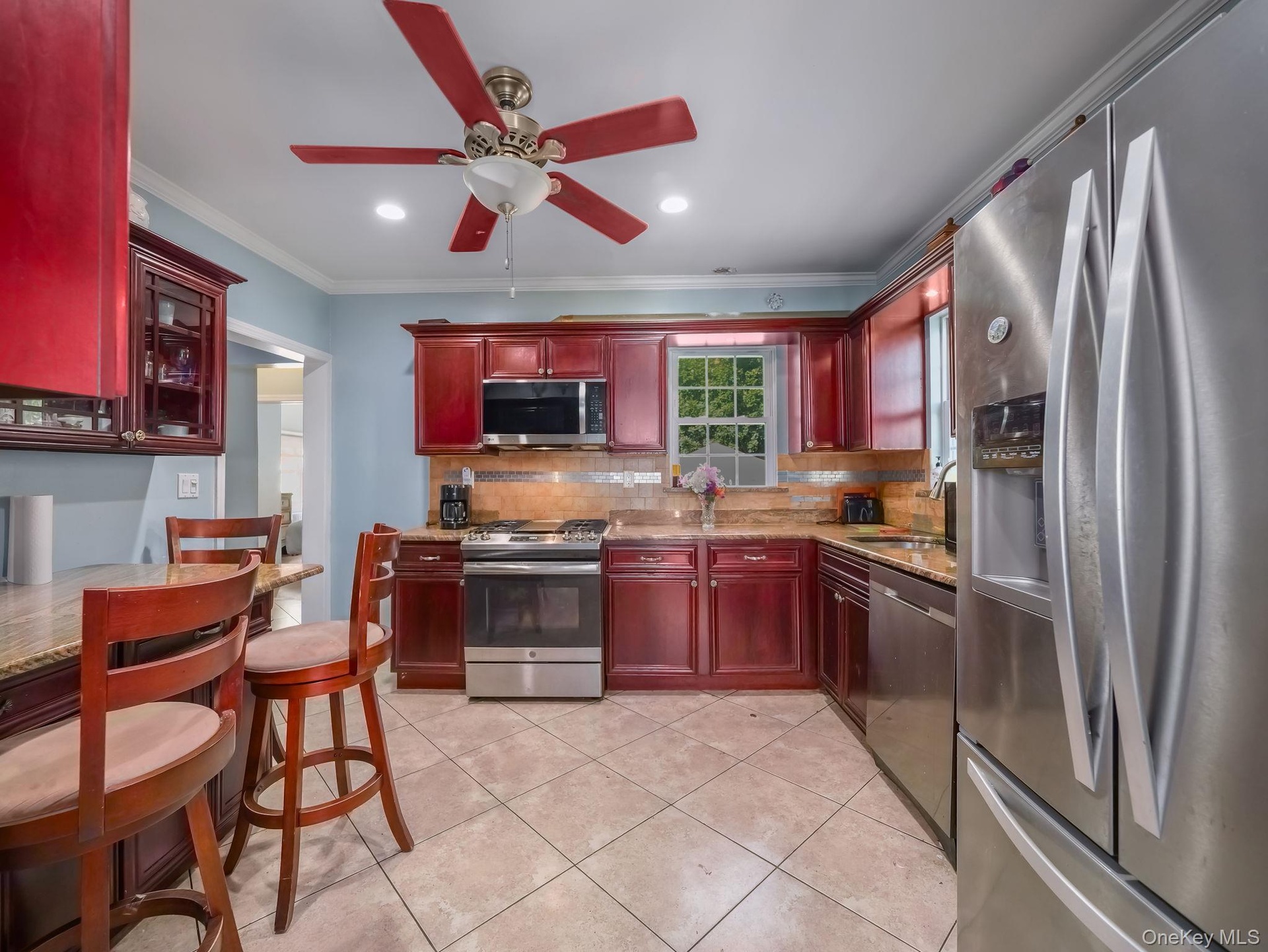 Kitchen with dark brown cabinets, stainless steel appliances, light stone countertops, ornamental molding, and backsplash