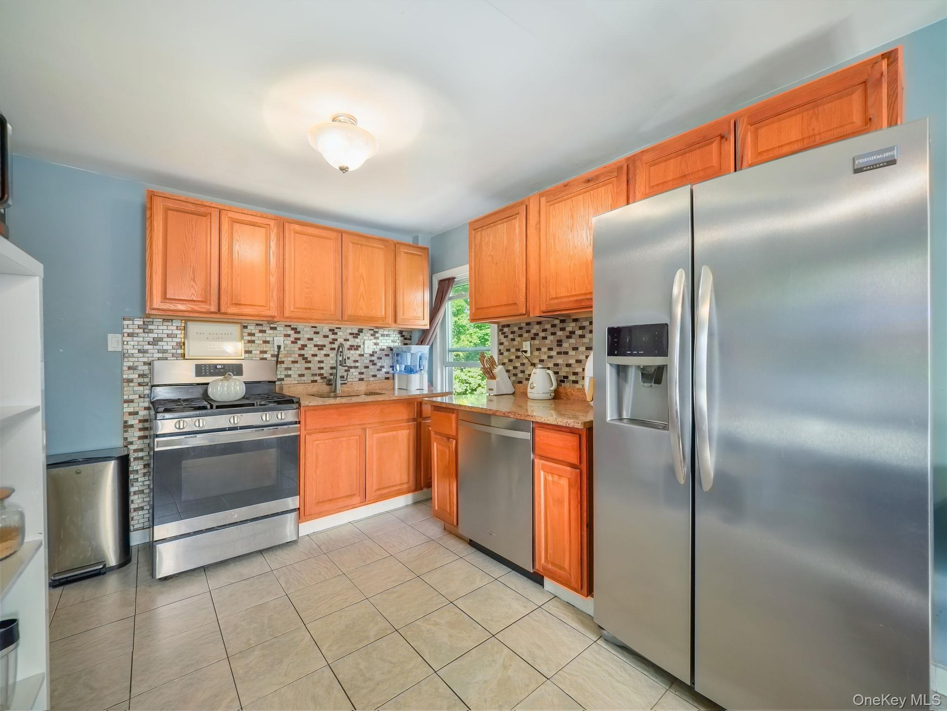 Kitchen featuring appliances with stainless steel finishes, decorative backsplash, light tile patterned flooring, light stone counters, and brown cabi