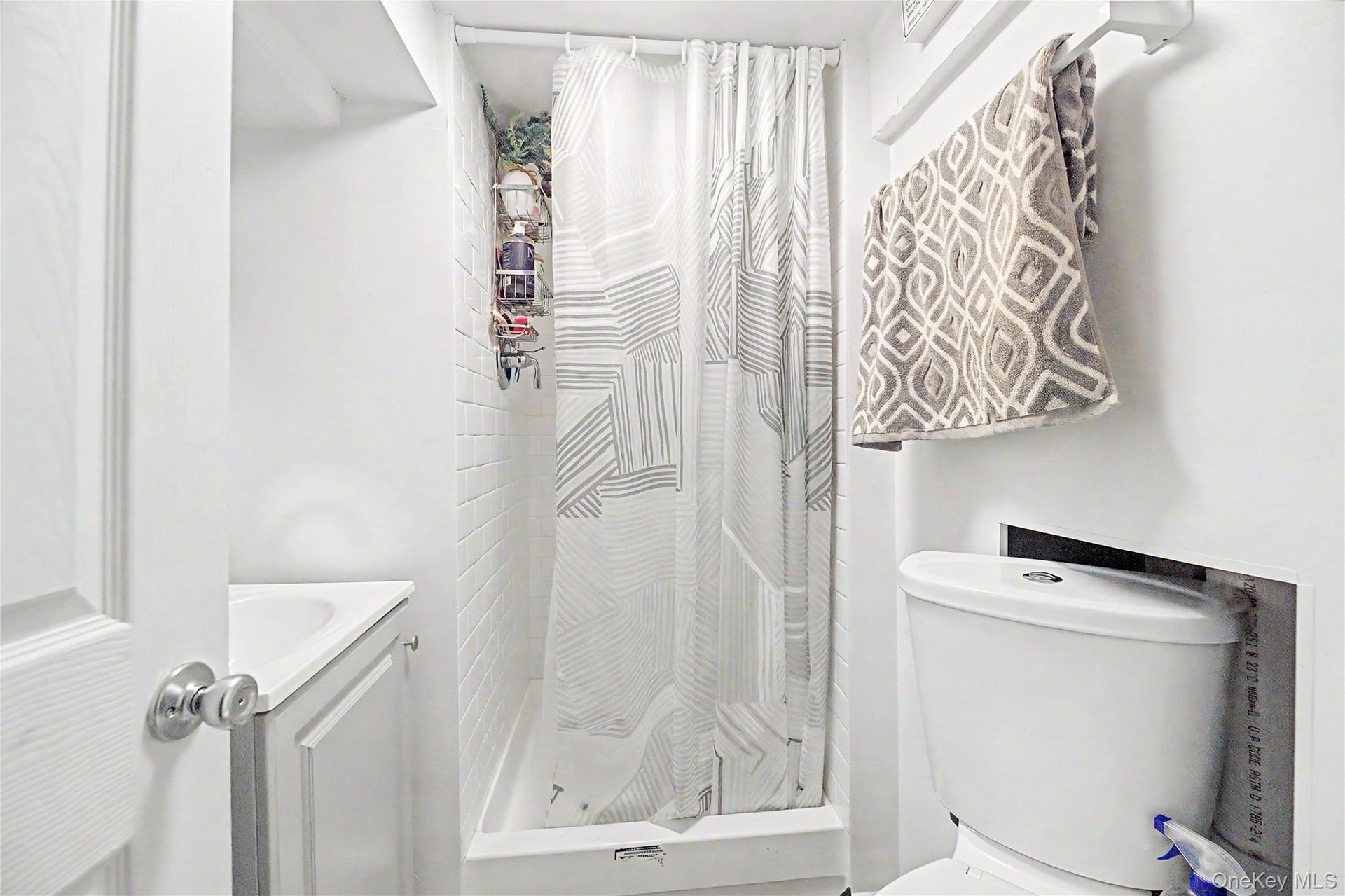 Shower with white subway tile surround, white shower pan, white vanity with integrated sink, and white toilet
