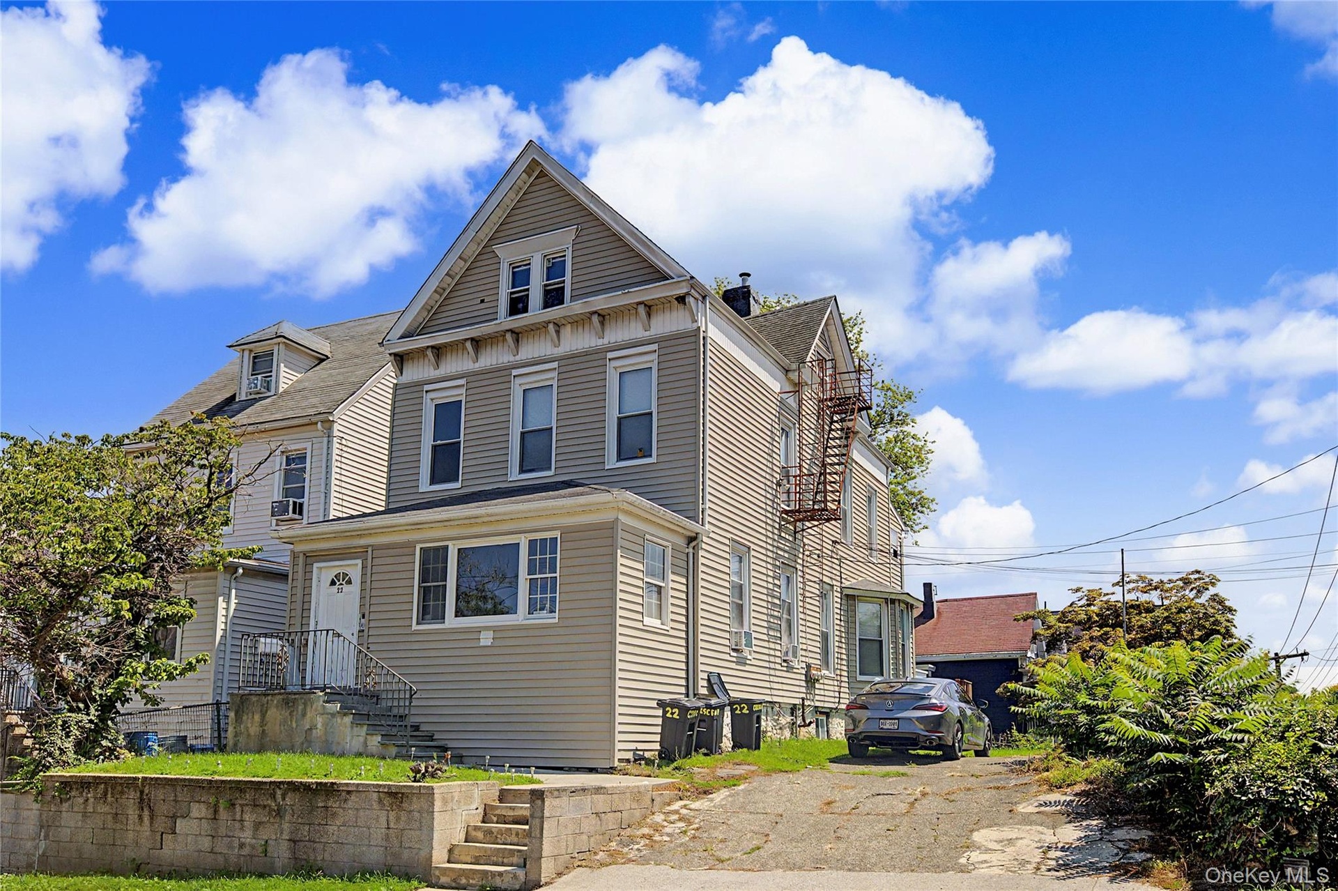 Vinyl siding exterior with a pitched roof, front entry with steps, paved driveway, and established plantings