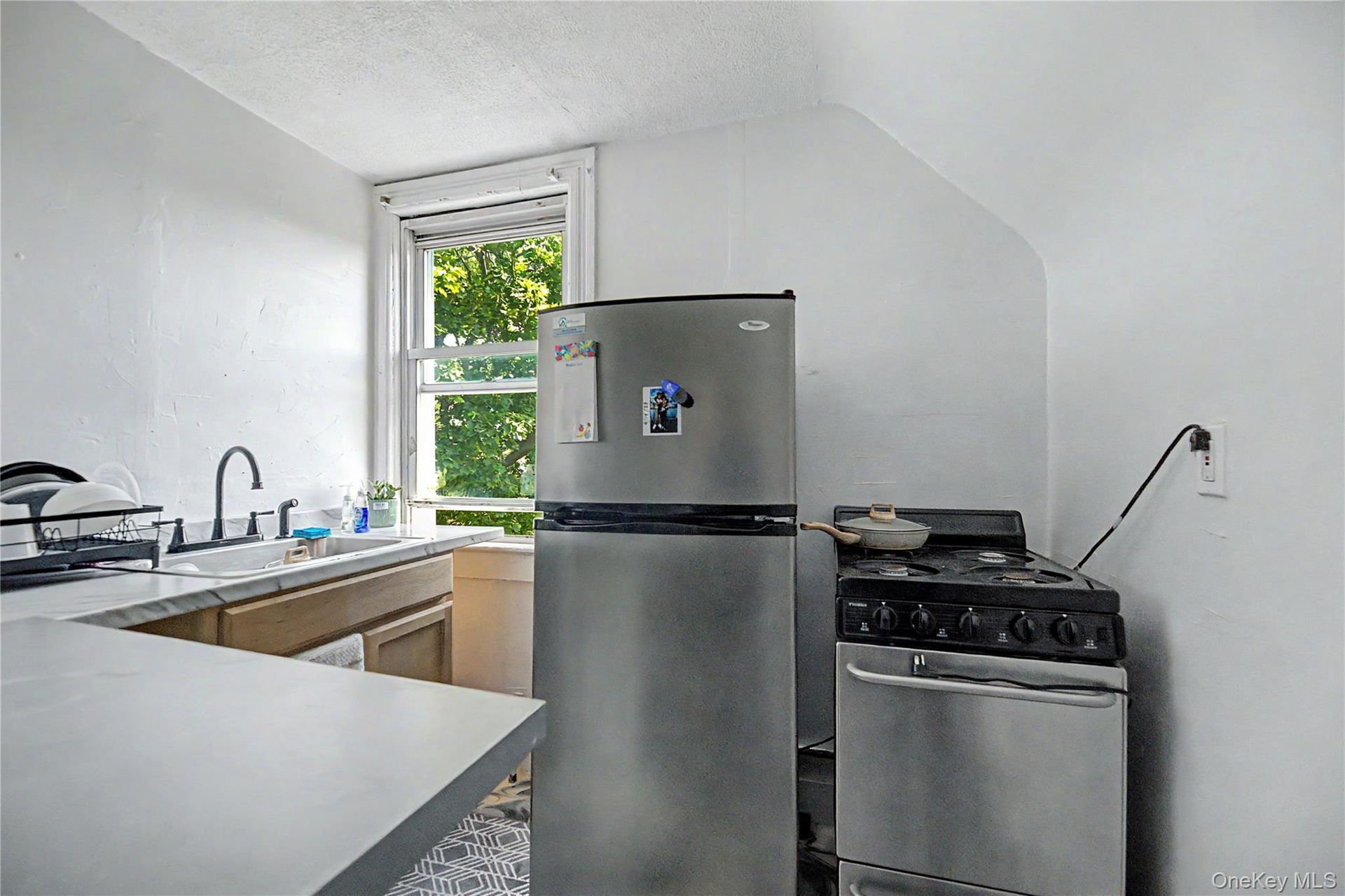 White walls with a window, stainless steel refrigerator, and stainless steel range
