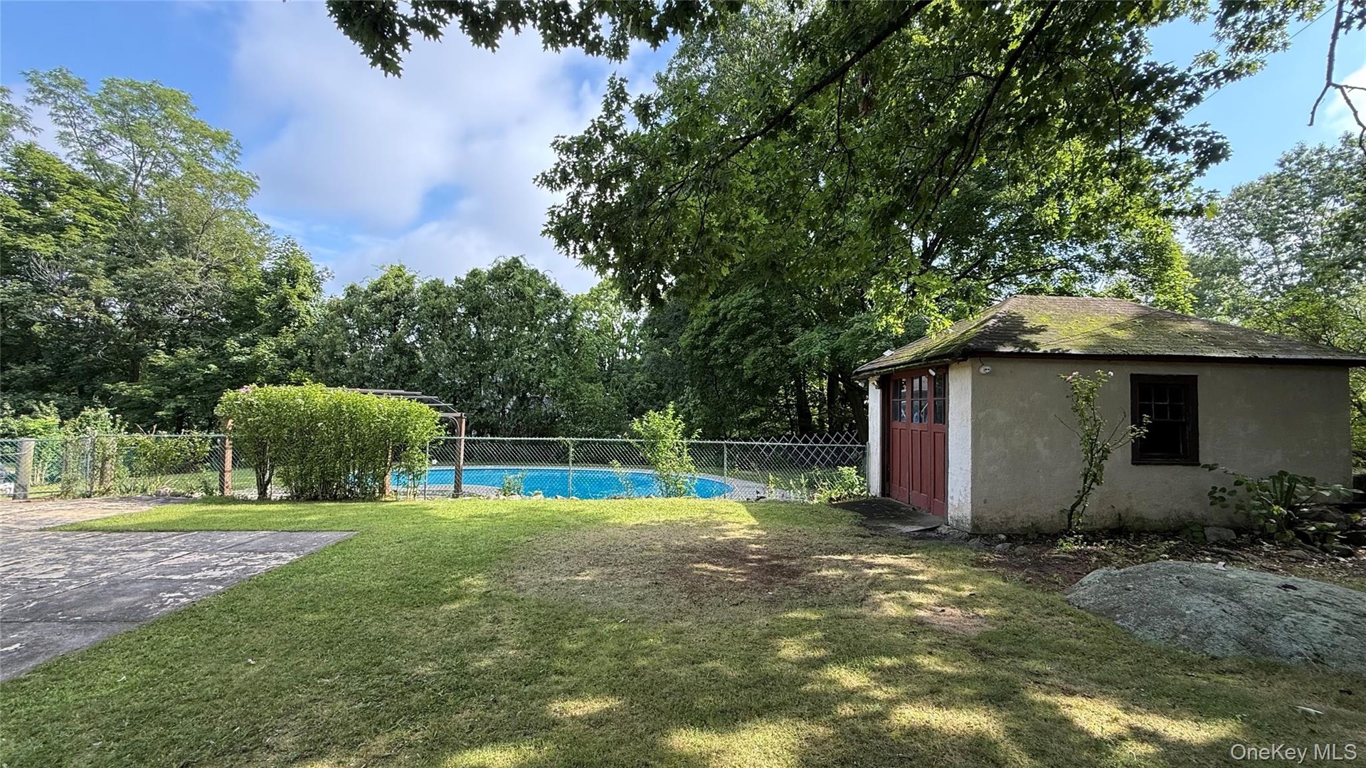 Fenced swimming pool, detached stucco structure, mature trees, green lawn, natural rock elements