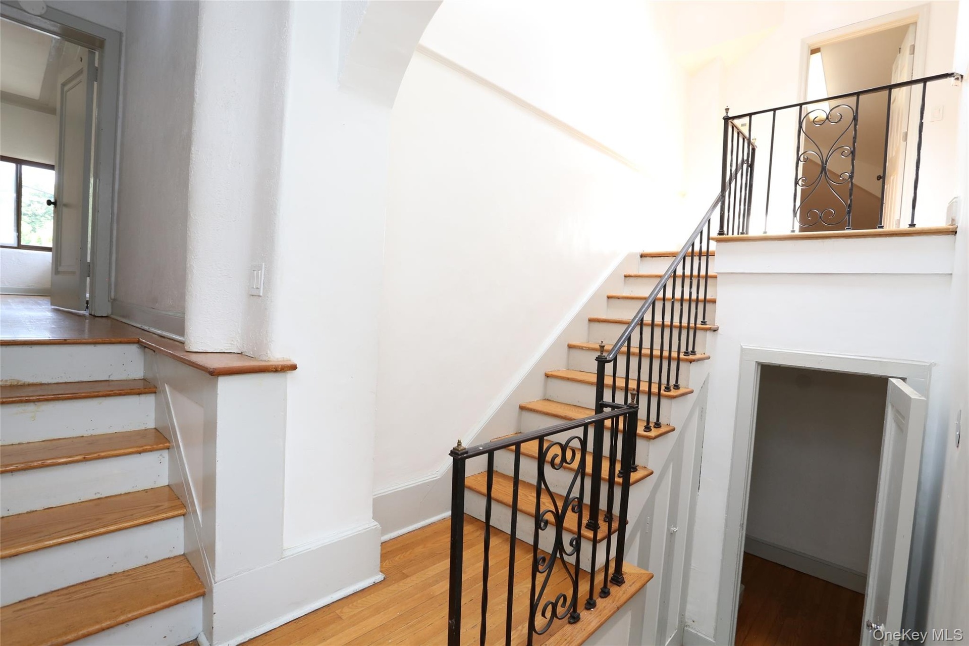 Hardwood flooring throughout, featuring a staircase with wrought iron railings and wood treads