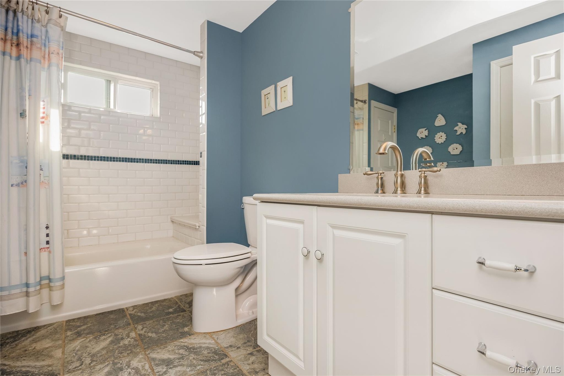 White subway tile shower surround with a decorative accent band, built-in tub, and a vanity with a light-colored countertop
