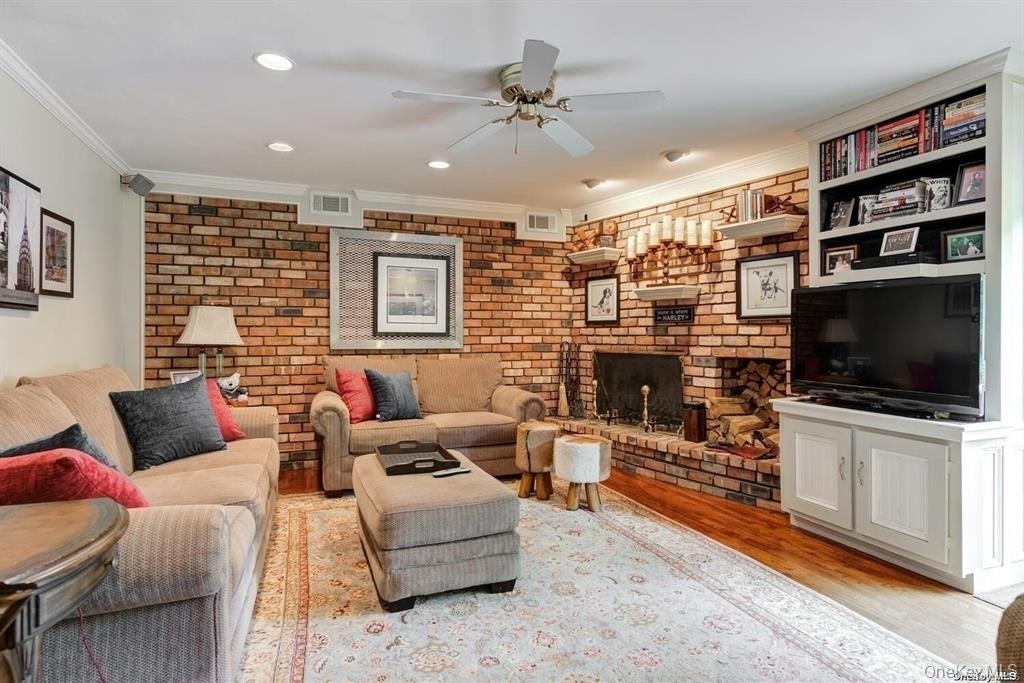 Living area featuring light wood-type flooring, crown molding, brick wall, a fireplace, and a ceiling fan
