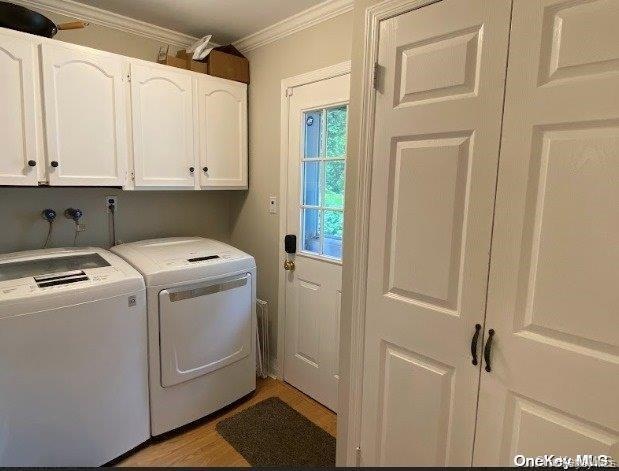 Laundry room with cabinet space, washer and dryer, ornamental molding, and light wood-style floors