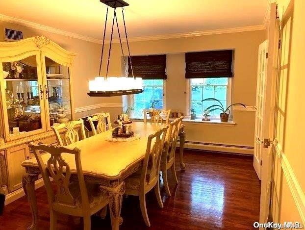 Dining area with a baseboard heating unit, dark wood-type flooring, and ornamental molding