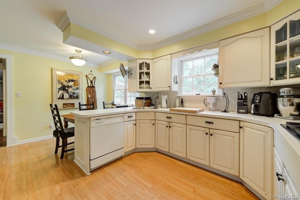 Kitchen featuring white dishwasher, a peninsula, a kitchen breakfast bar, glass insert cabinets, and backsplash