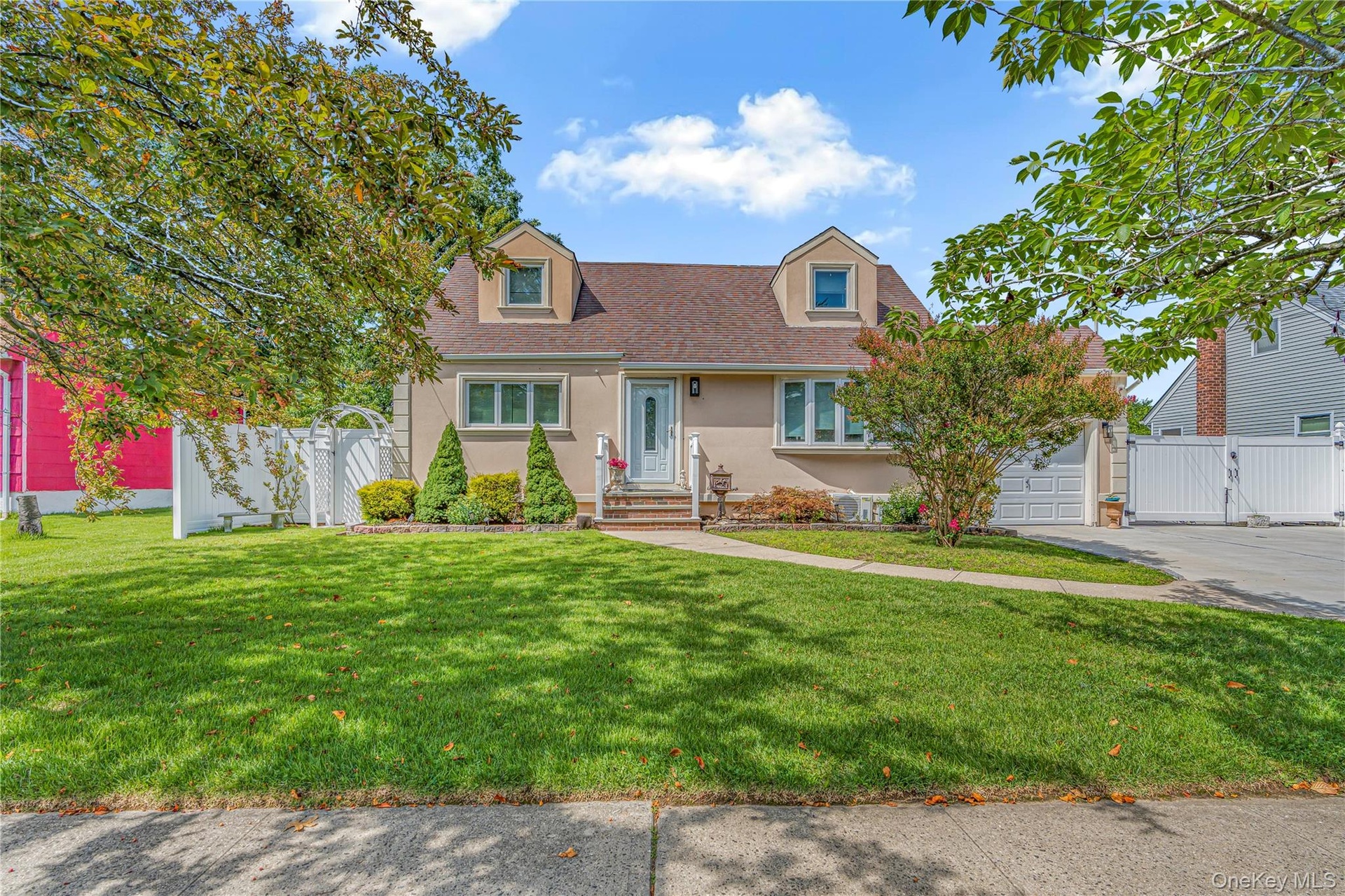 Stucco exterior with dormer windows, a concrete driveway, and a white fence