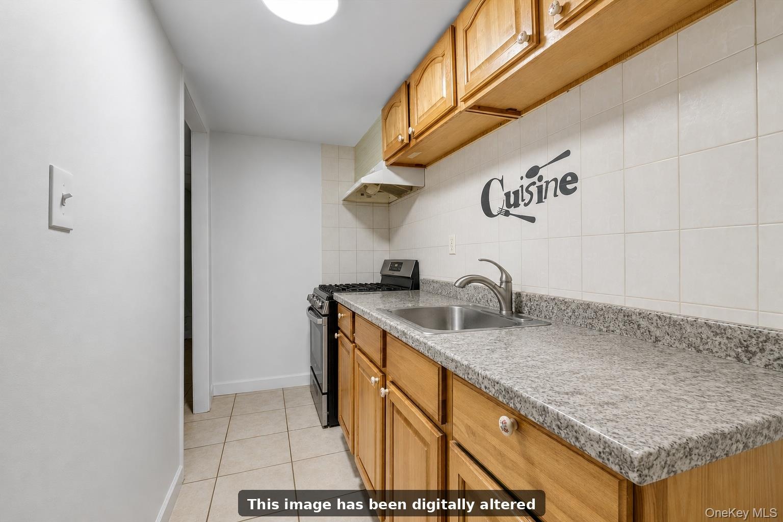 Galley kitchen featuring wood-finish cabinetry, speckled stone countertops, stainless steel sink with faucet, ceramic tile backsplash, and tile floori
