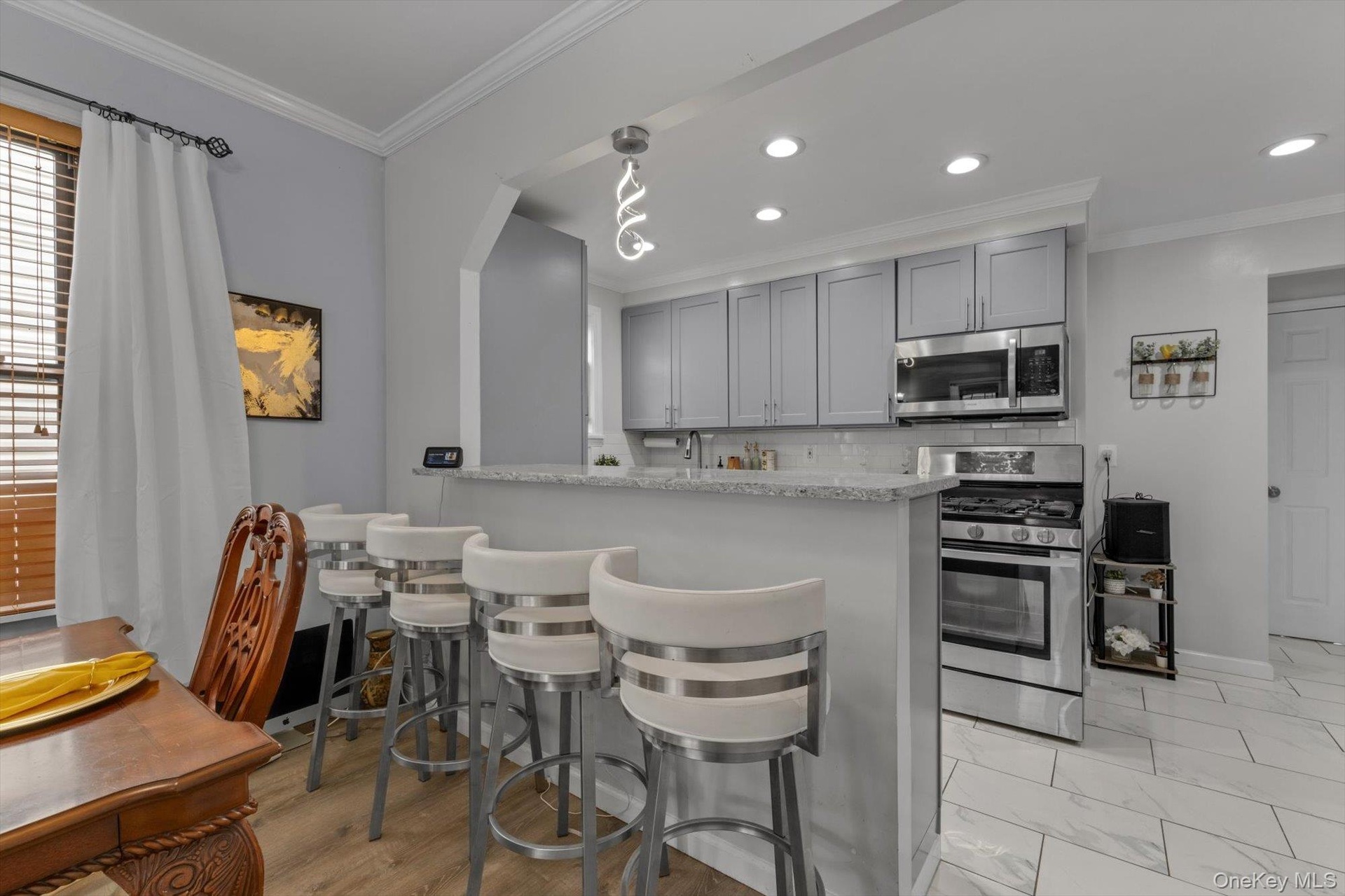 Kitchen featuring light gray cabinetry, stainless steel appliances, recessed lighting, and a breakfast bar.