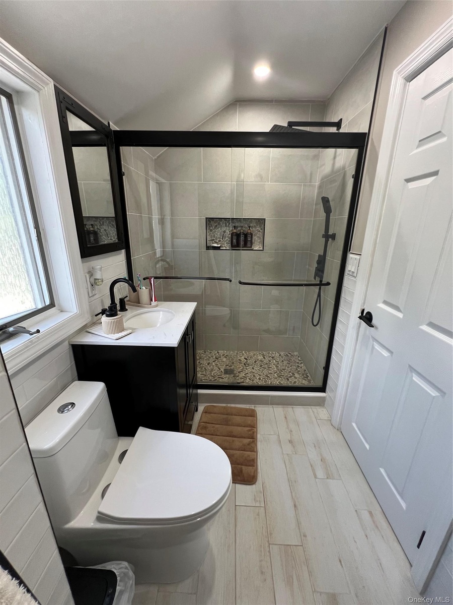 Modern bathroom featuring a glass-enclosed shower with pebble-finish flooring, a contemporary vanity with a white countertop and rectangular sink, and