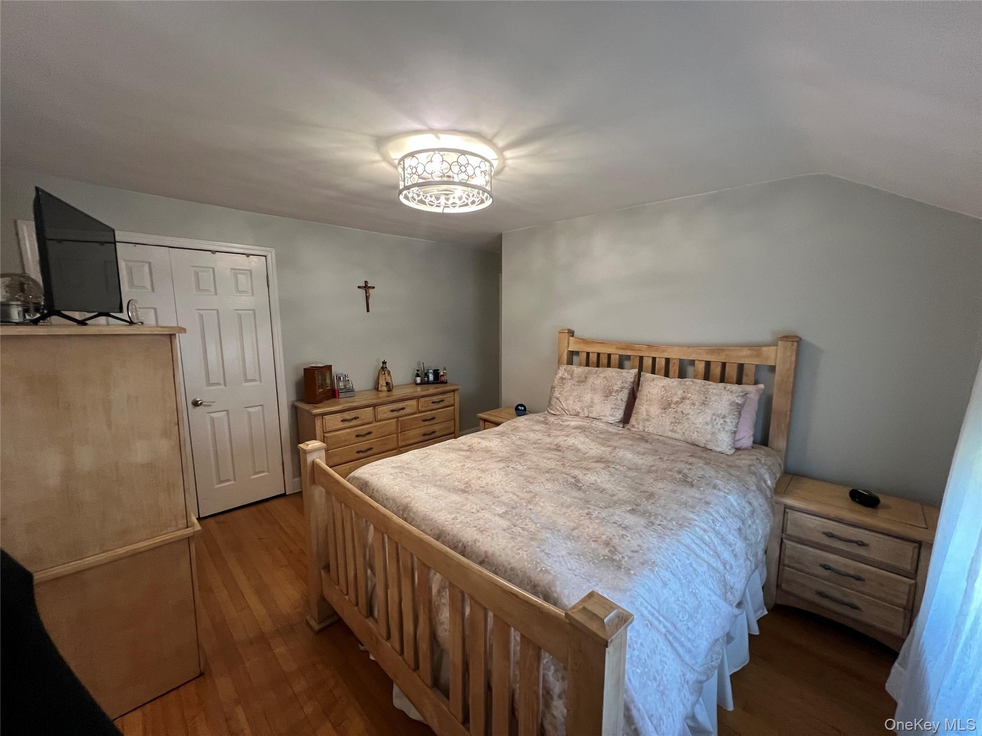 Hardwood flooring, overhead ceiling light fixture, white interior door, light-toned walls, and sloped ceiling detail