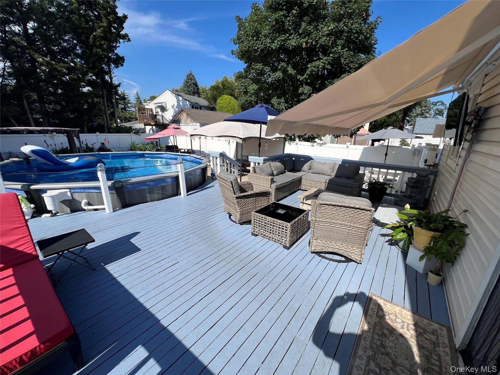 Expansive wood deck with an above-ground pool, a retractable awning, and white railing